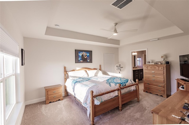 bedroom featuring ensuite bathroom, ceiling fan, light carpet, and a raised ceiling