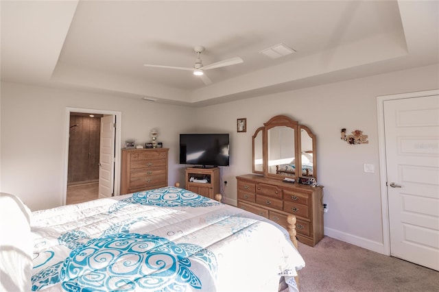 carpeted bedroom with ensuite bathroom, ceiling fan, and a tray ceiling