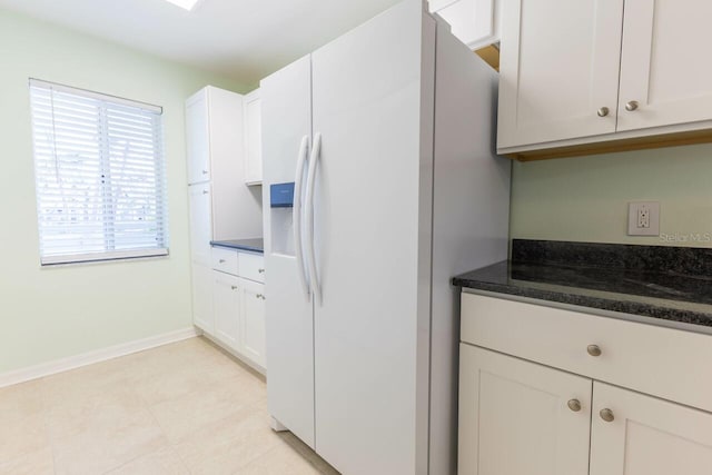 kitchen featuring dark stone countertops, white fridge with ice dispenser, and white cabinets