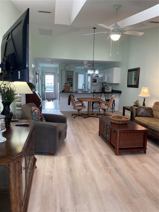 living room with ceiling fan with notable chandelier, light hardwood / wood-style floors, and a high ceiling