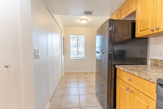 kitchen with light stone counters, black refrigerator, and light tile patterned flooring