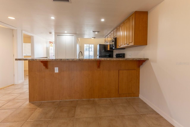 kitchen with kitchen peninsula, black refrigerator, light tile patterned floors, and sink