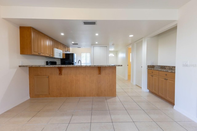 kitchen with black fridge, kitchen peninsula, light stone counters, and light tile patterned floors