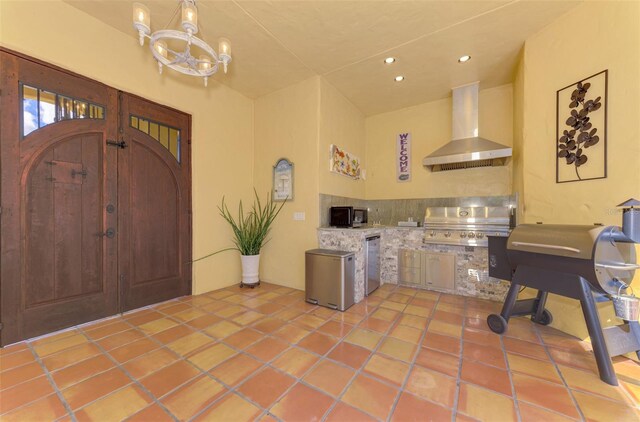 kitchen with a chandelier, appliances with stainless steel finishes, light tile patterned floors, and wall chimney exhaust hood