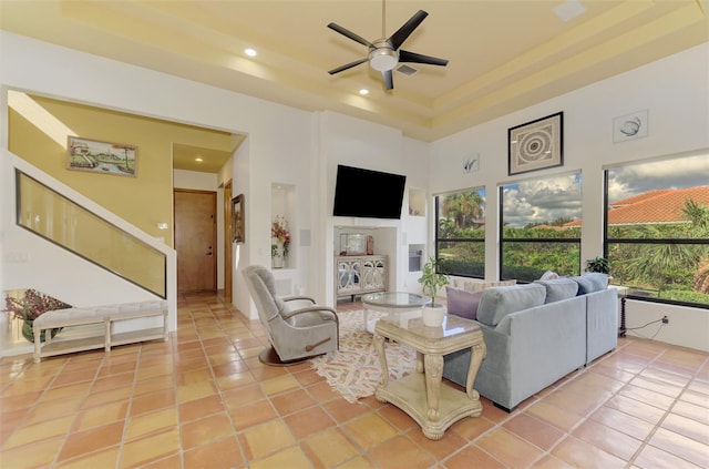 living room with ceiling fan, light tile patterned flooring, a raised ceiling, and a high ceiling