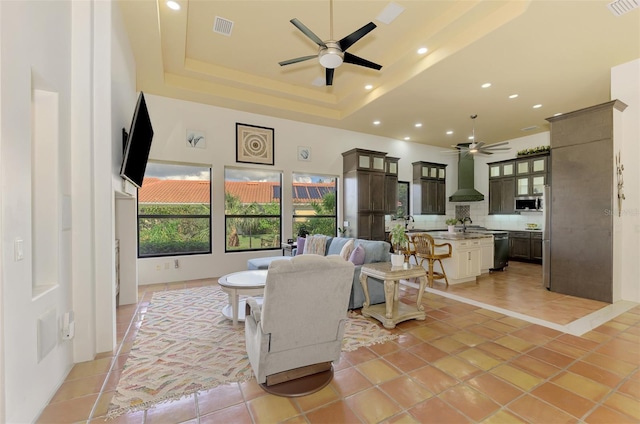 tiled living room with a raised ceiling, ceiling fan, and a high ceiling