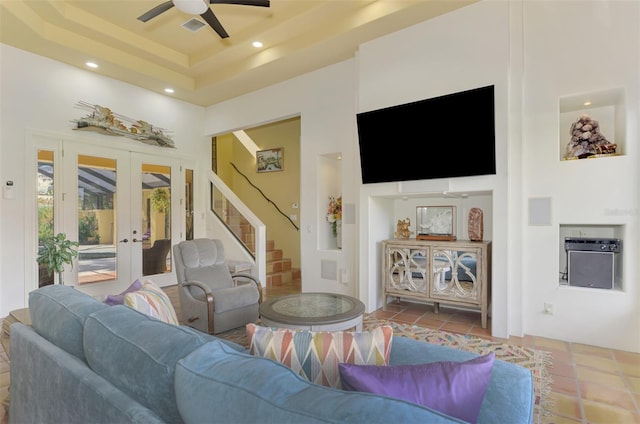 tiled living room featuring ceiling fan, a raised ceiling, a high ceiling, and french doors