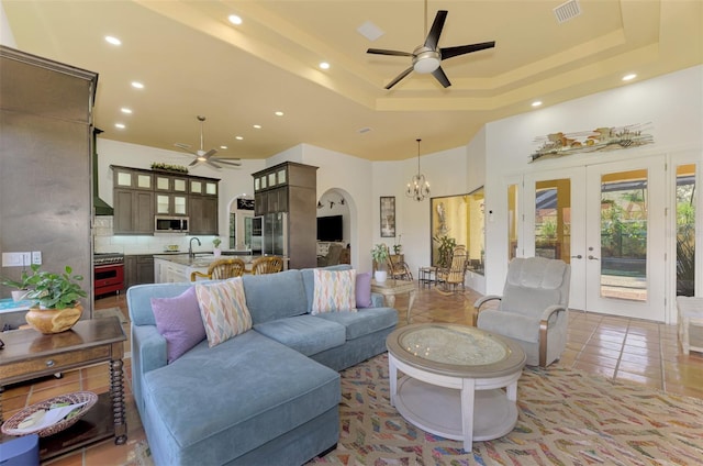 tiled living room featuring a tray ceiling, french doors, ceiling fan with notable chandelier, and sink