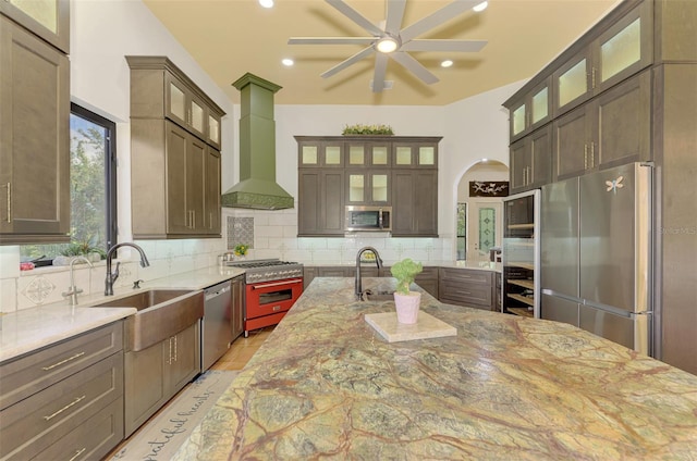 kitchen with a kitchen island with sink, sink, appliances with stainless steel finishes, tasteful backsplash, and light stone counters