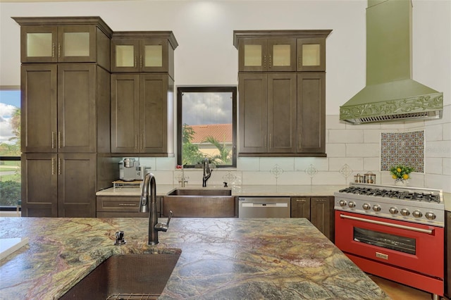 kitchen featuring decorative backsplash, appliances with stainless steel finishes, light stone counters, wall chimney exhaust hood, and sink