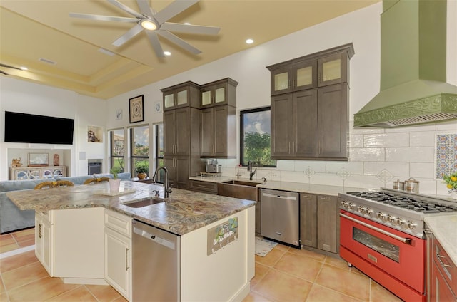 kitchen featuring wall chimney exhaust hood, sink, a kitchen island with sink, and appliances with stainless steel finishes