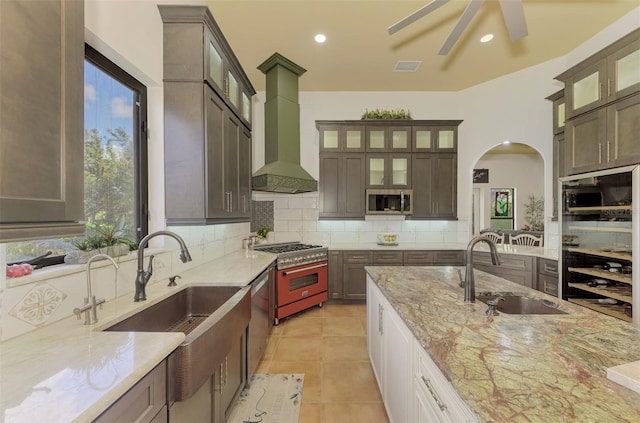 kitchen with backsplash, wall chimney range hood, sink, light stone countertops, and appliances with stainless steel finishes