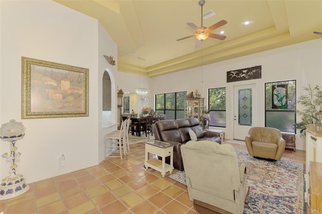 tiled living room with a tray ceiling, ceiling fan, and a towering ceiling