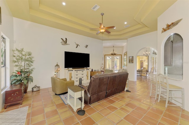 tiled living room featuring a high ceiling, ceiling fan with notable chandelier, and a tray ceiling