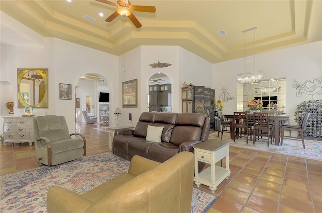 living room with tile patterned flooring, a high ceiling, ceiling fan with notable chandelier, and a raised ceiling