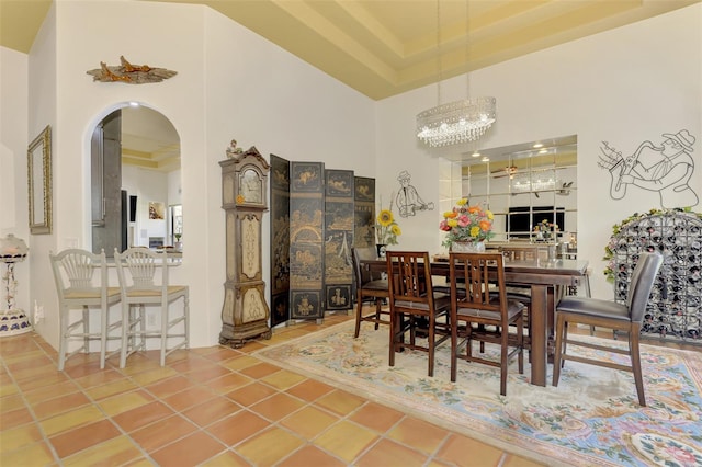 dining space with tile patterned flooring, a high ceiling, a chandelier, and a raised ceiling