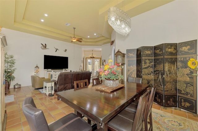 dining space with a tray ceiling, light tile patterned floors, and ceiling fan with notable chandelier