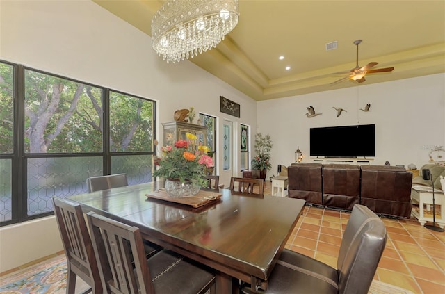 tiled dining room with ceiling fan with notable chandelier and a tray ceiling