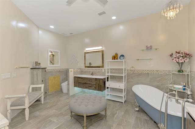 bathroom with a bathing tub, vanity, toilet, and tile walls