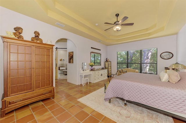 tiled bedroom with a barn door, a tray ceiling, and ceiling fan