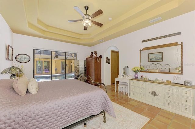 tiled bedroom featuring ceiling fan, access to exterior, and a tray ceiling