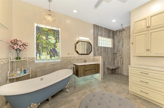 bathroom with ceiling fan, vanity, tile walls, and shower with separate bathtub