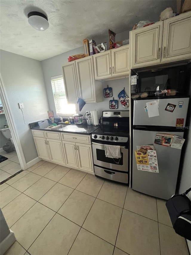 kitchen featuring cream cabinets, light tile patterned flooring, stainless steel appliances, a textured ceiling, and sink