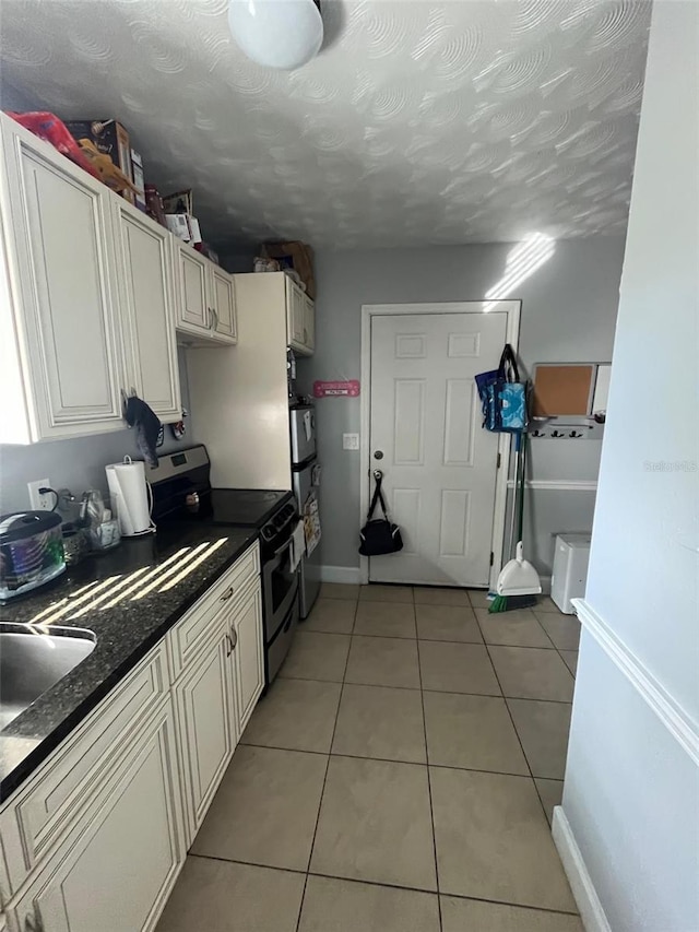 kitchen with appliances with stainless steel finishes, sink, light tile patterned floors, and a textured ceiling