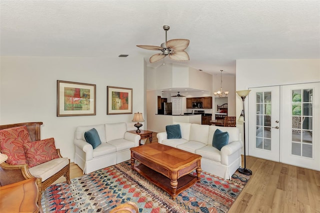 living room with lofted ceiling, ceiling fan with notable chandelier, french doors, and light hardwood / wood-style flooring