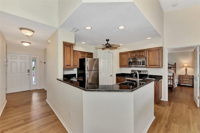 kitchen featuring dark stone countertops, light wood-type flooring, kitchen peninsula, and stainless steel appliances