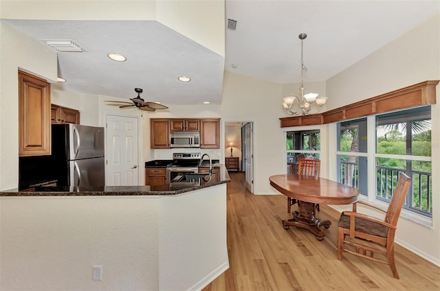 kitchen with kitchen peninsula, appliances with stainless steel finishes, dark stone counters, light hardwood / wood-style flooring, and pendant lighting