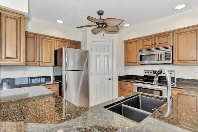 kitchen with sink, appliances with stainless steel finishes, ceiling fan, dark stone countertops, and a textured ceiling