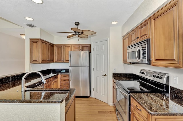 kitchen featuring kitchen peninsula, stainless steel appliances, light hardwood / wood-style floors, and dark stone countertops