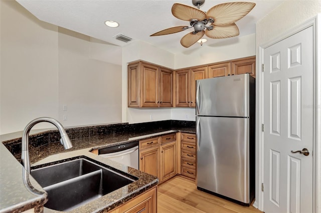 kitchen featuring light wood-type flooring, appliances with stainless steel finishes, sink, dark stone countertops, and ceiling fan