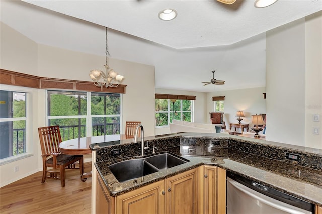 kitchen featuring ceiling fan with notable chandelier, sink, stainless steel dishwasher, light wood-type flooring, and dark stone countertops