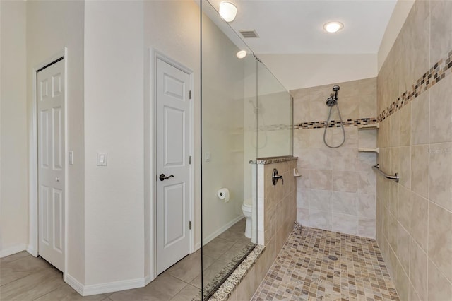 bathroom featuring lofted ceiling, tile patterned flooring, toilet, and a tile shower