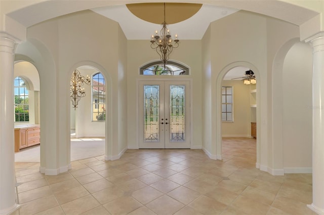 tiled foyer with decorative columns, french doors, a high ceiling, and ceiling fan with notable chandelier