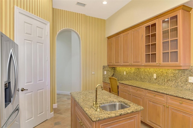 kitchen with a center island with sink, stainless steel fridge, light stone countertops, and sink