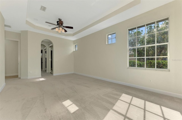 empty room featuring ceiling fan, light carpet, and a tray ceiling