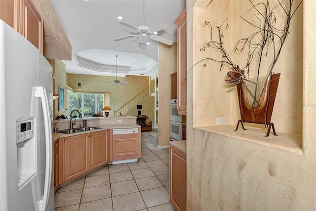 kitchen with ornamental molding, a raised ceiling, ceiling fan, sink, and white refrigerator with ice dispenser