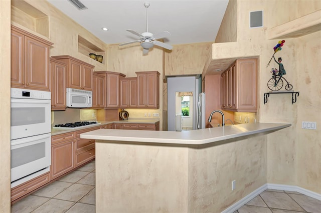 kitchen with kitchen peninsula, white appliances, ceiling fan, light tile patterned floors, and a high ceiling