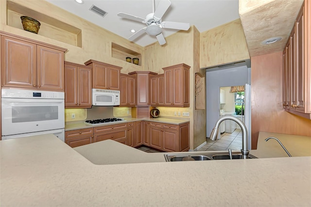 kitchen featuring white appliances, sink, ceiling fan, a towering ceiling, and light tile patterned flooring