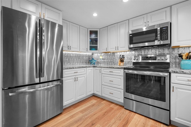 kitchen with light wood-type flooring, white cabinets, light stone counters, and stainless steel appliances