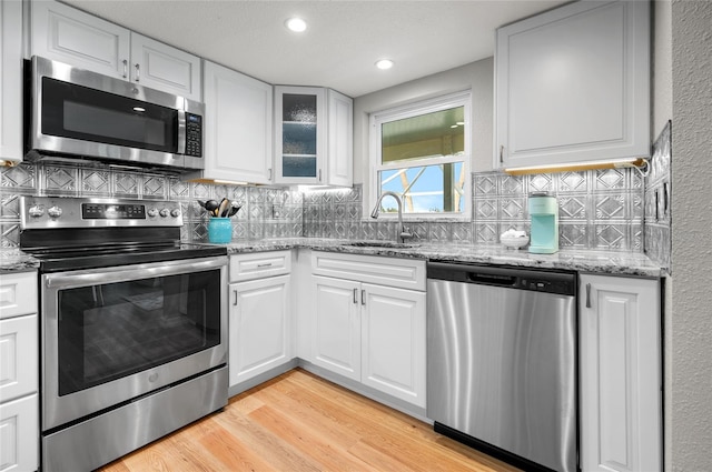 kitchen with stainless steel appliances, white cabinets, sink, and light hardwood / wood-style flooring