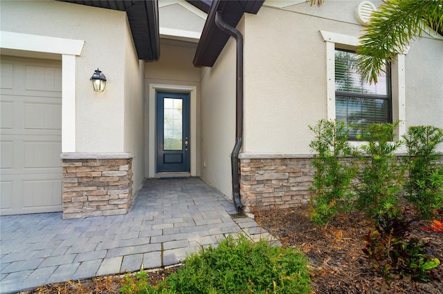 view of exterior entry with stucco siding, stone siding, and an attached garage