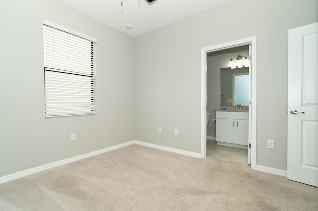 unfurnished bedroom featuring a sink, baseboards, light carpet, and connected bathroom