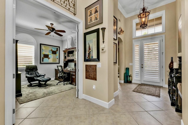 foyer with a wealth of natural light, light tile patterned flooring, crown molding, and ceiling fan