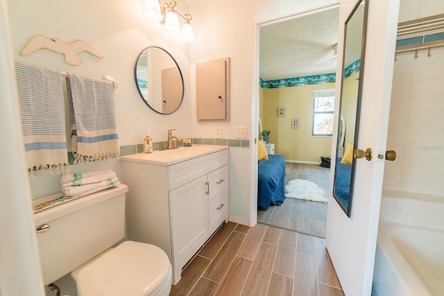 bathroom with toilet, vanity, a textured ceiling, and a tub to relax in