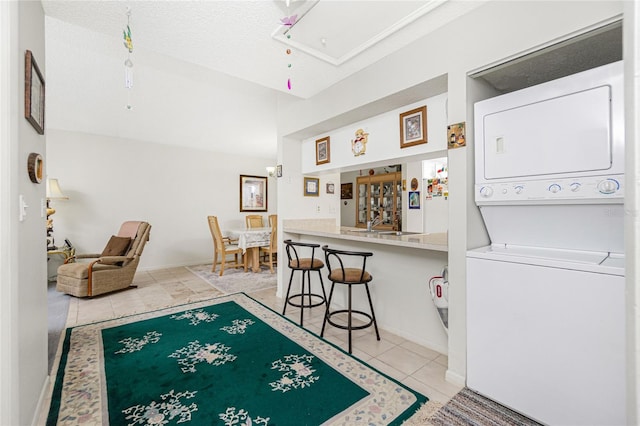 interior space with light tile patterned flooring, stacked washer and clothes dryer, a textured ceiling, and a kitchen breakfast bar