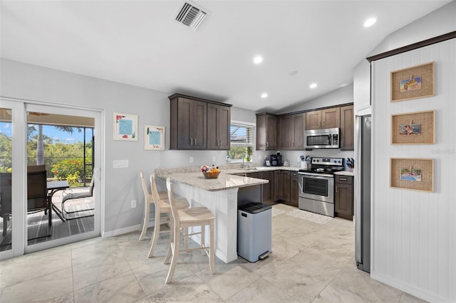 kitchen with a breakfast bar, vaulted ceiling, light stone countertops, appliances with stainless steel finishes, and kitchen peninsula